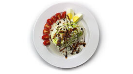 A wedge salad drizzled with balsamic vinegar with sliced cherry tomatoes on the side